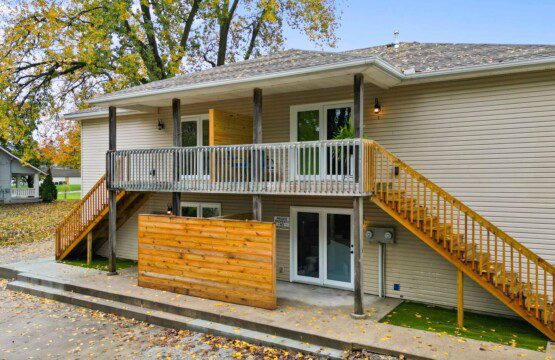 Two-story beige building with exterior staircases, upper balcony, and autumn leaves on the ground.