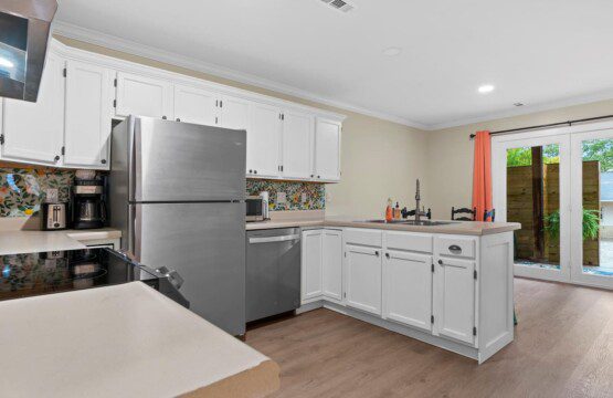 Bright kitchen with white cabinets, stainless steel refrigerator and dishwasher, electric stove, patterned backsplash, and glass doors leading to an outdoor patio.